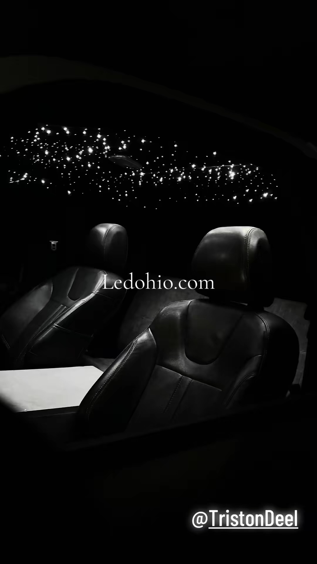 White fiber-optic starlight headliner glowing above black leather car seats